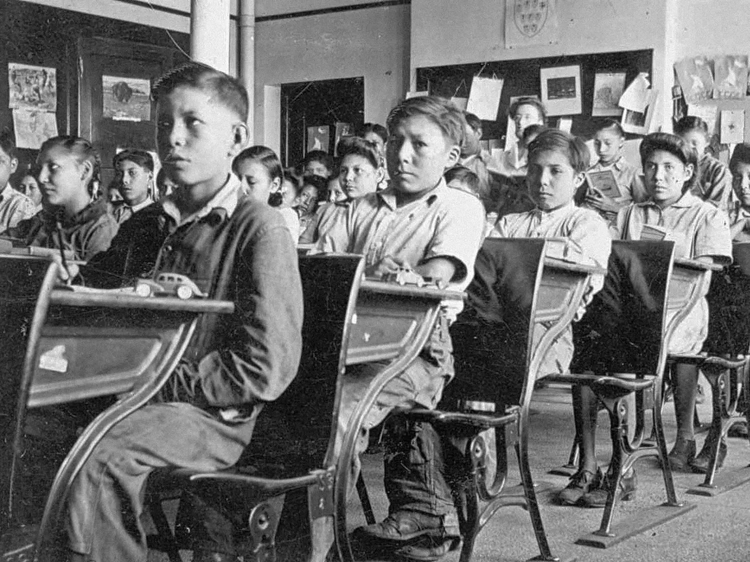 Rows of elementary school students sit in a packed classroom.