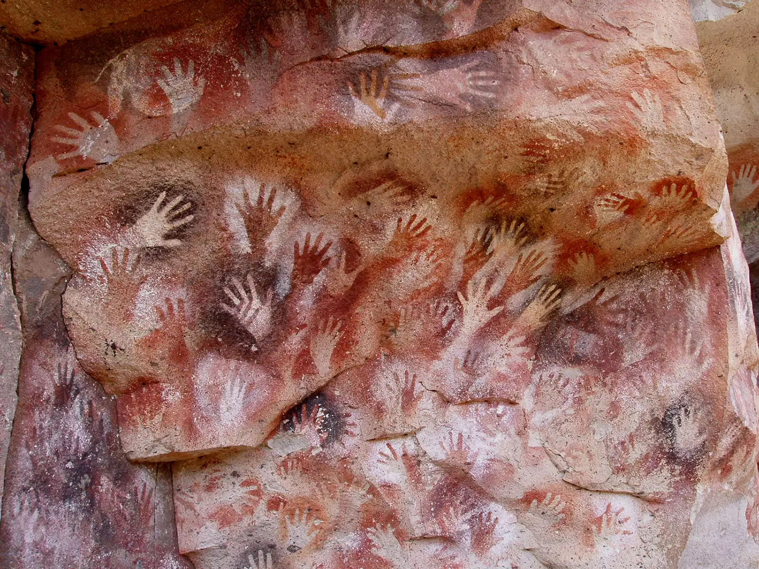 A cave wall covered with the painted outlines of hands.