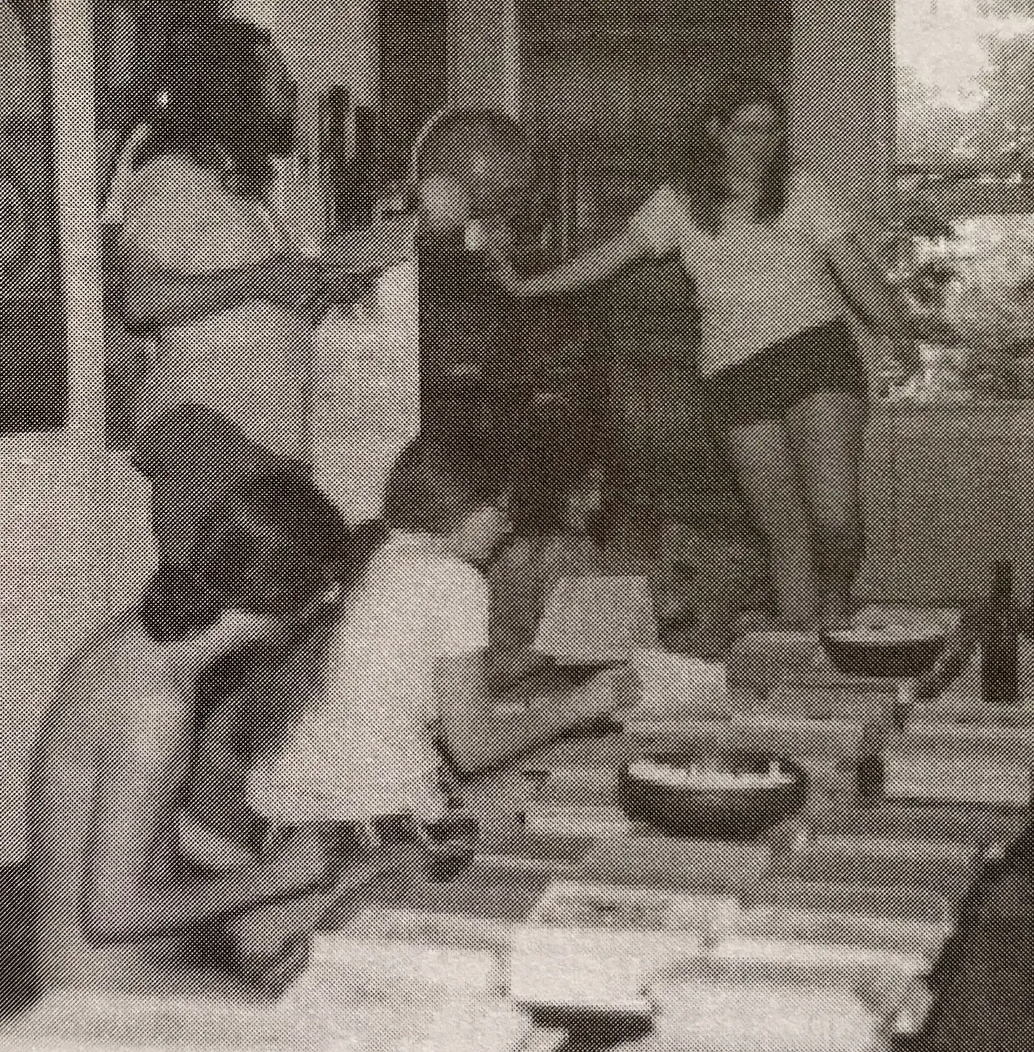 A group of people seated and standing in front of piles of papers. At least one of the workers appears to be nude.