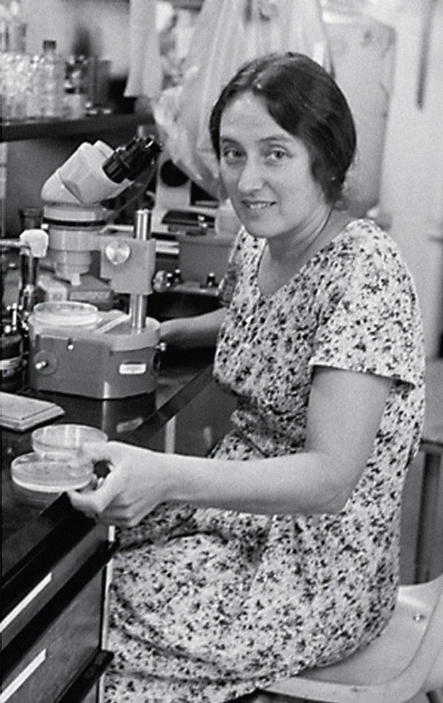 Portrait of Lynn Margulis at work in her laboratory, seated in front of a microscope.
