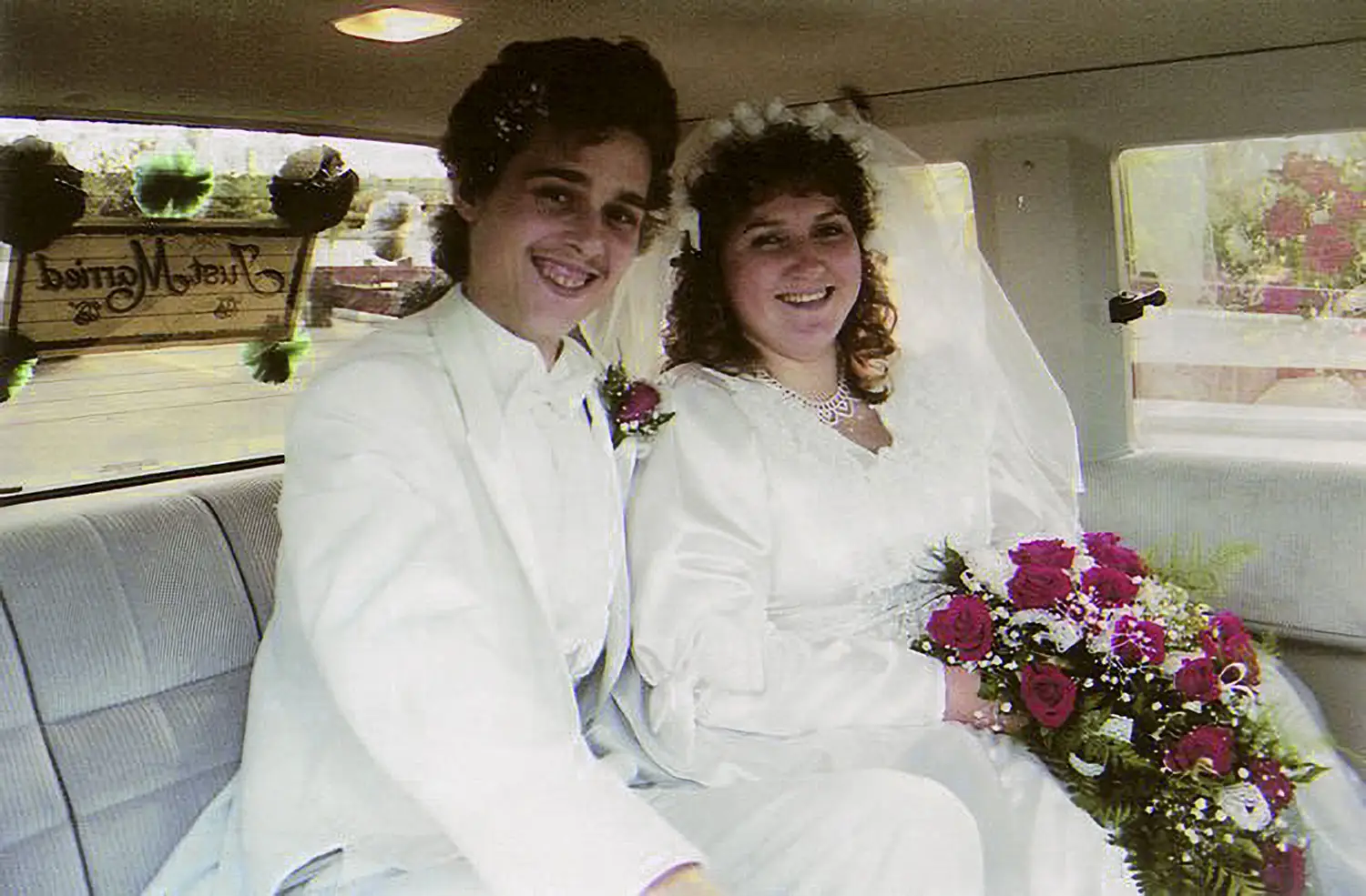 David and Jane are seen smiling in the back of a limousine. Both are dressed in white, smiling, and Jane is holding a bouquet.