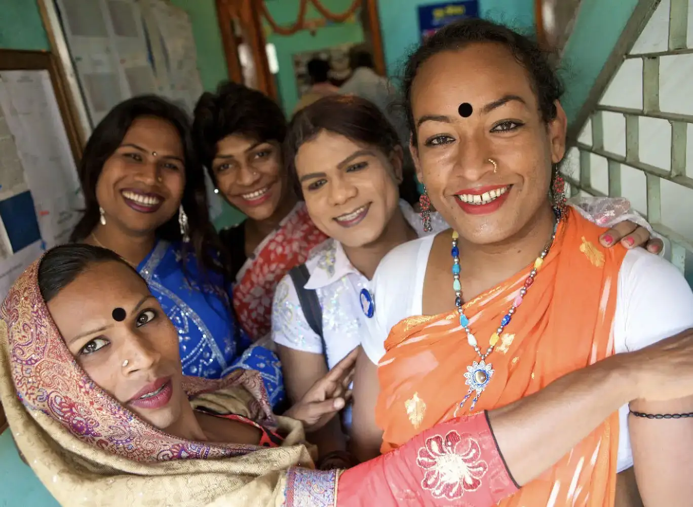 Five South Asian Hijras embracing each other for a group photo. They’re wearing colorful saris and smiling at the camera.