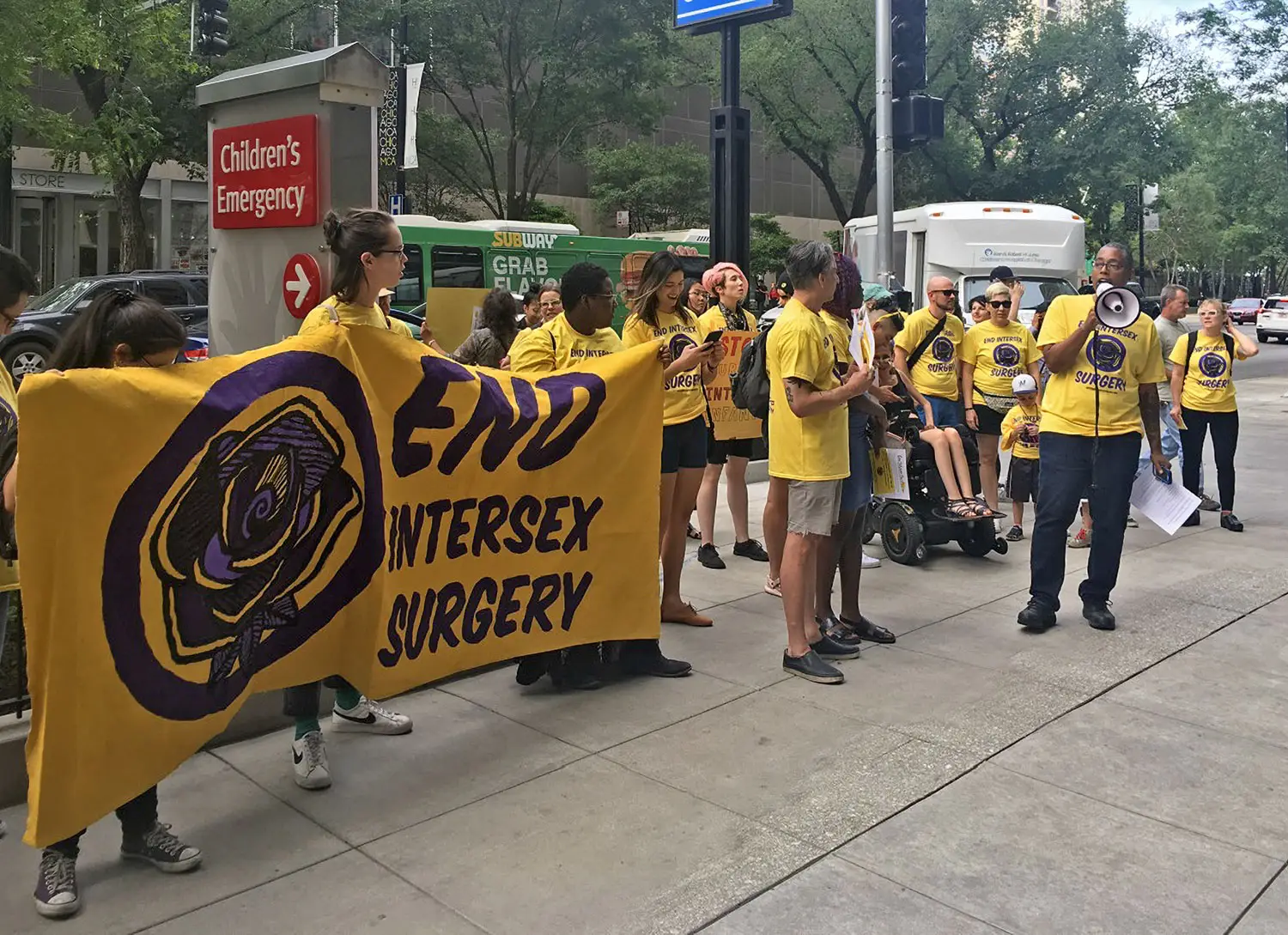 A group of activists standing outside a children’s hospital. They’re carrying a banner: “END intersex surgery.”