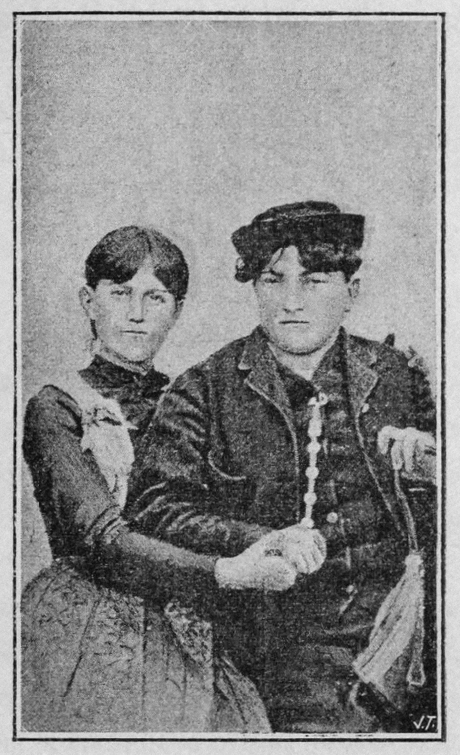 Two women. The woman on the right is dressed in traditional feminine clothing of the time, the one on the left has short hair and appears to be wearing masculine clothes. They embrace as they defiantly face the camera.