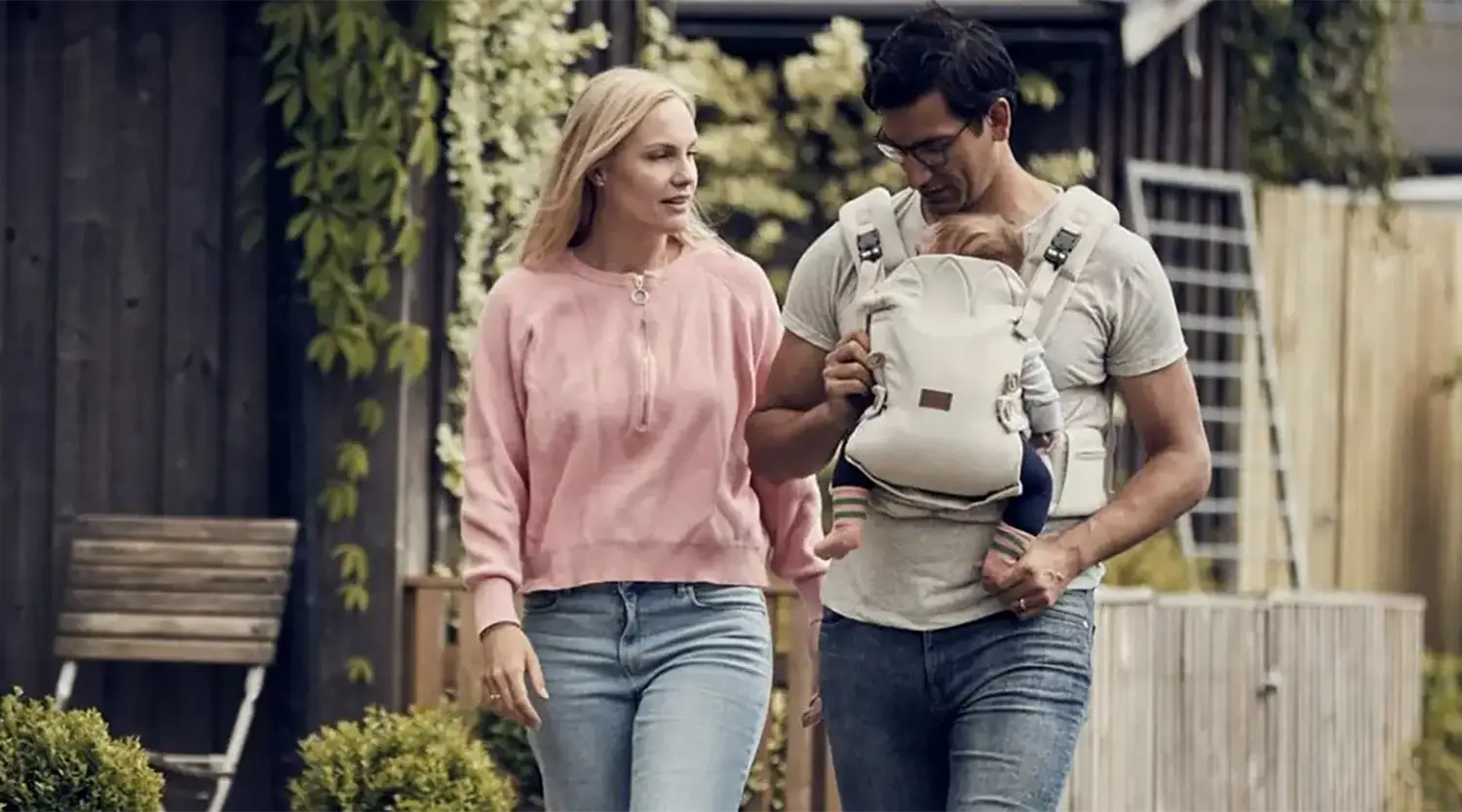 A man and woman walking together. The man is carrying a baby in a baby carrier strapped to his chest.
