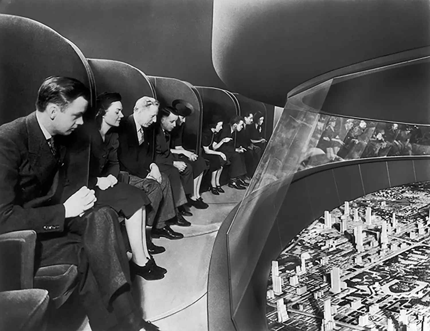 A group of people seated on a viewing platform, looking down at a model of a city.