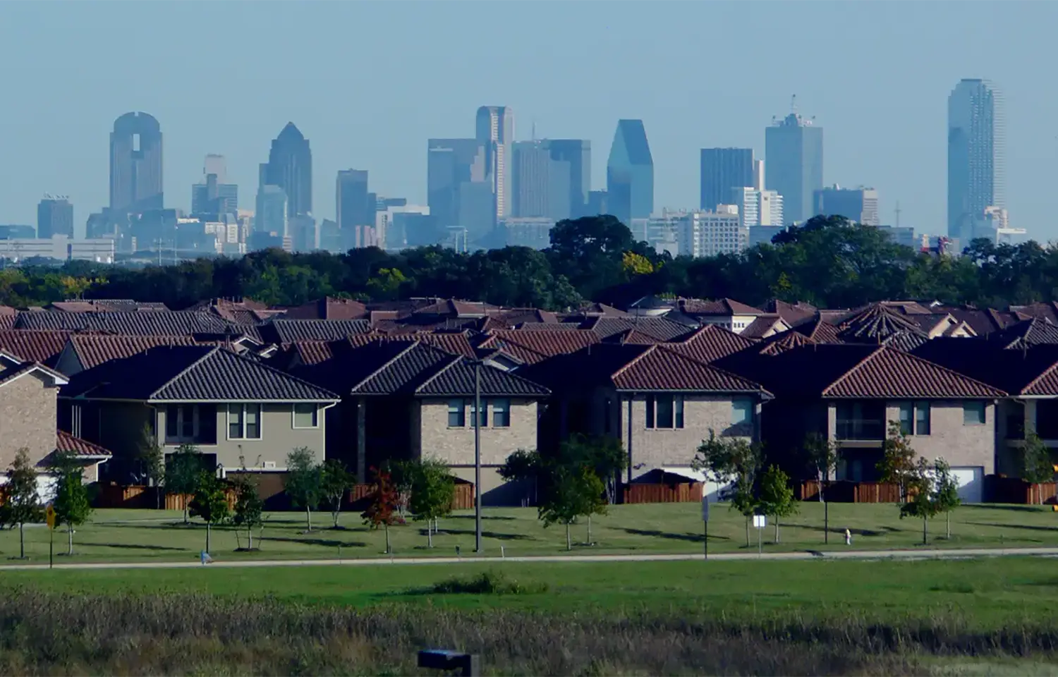 A landscape photo, in the foreground are rows of identical houses, and in the background are the highrises of the Dallas city skyline.