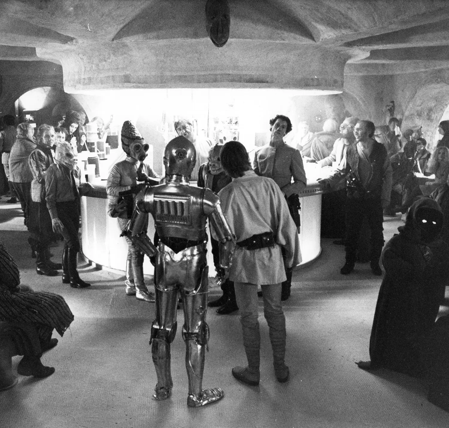 Luke and C3PO peer into a seedy bar filled with different kinds of alien types, who are staring back at them. 