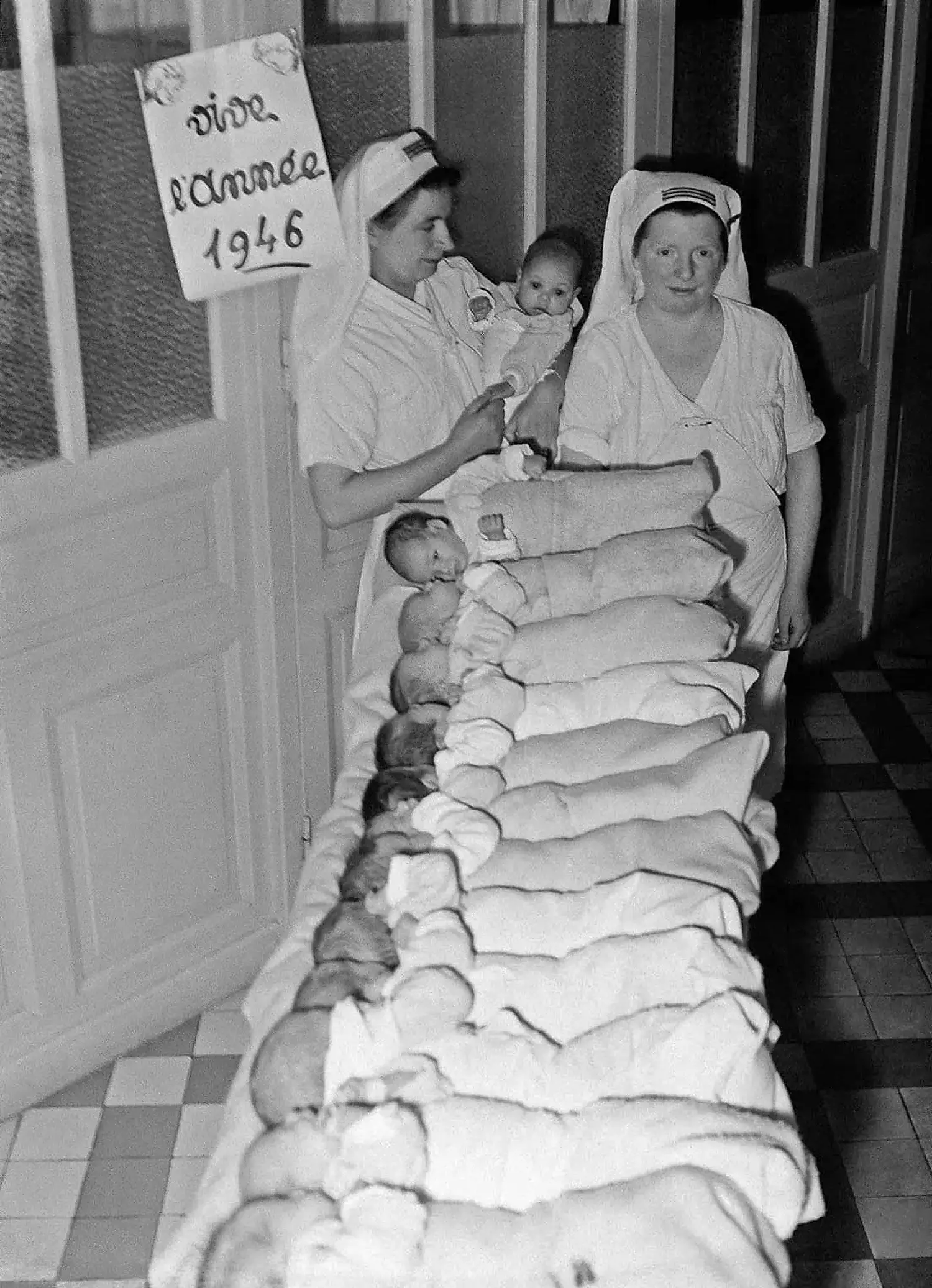 Two nurses proudly display 13 newborn babies.