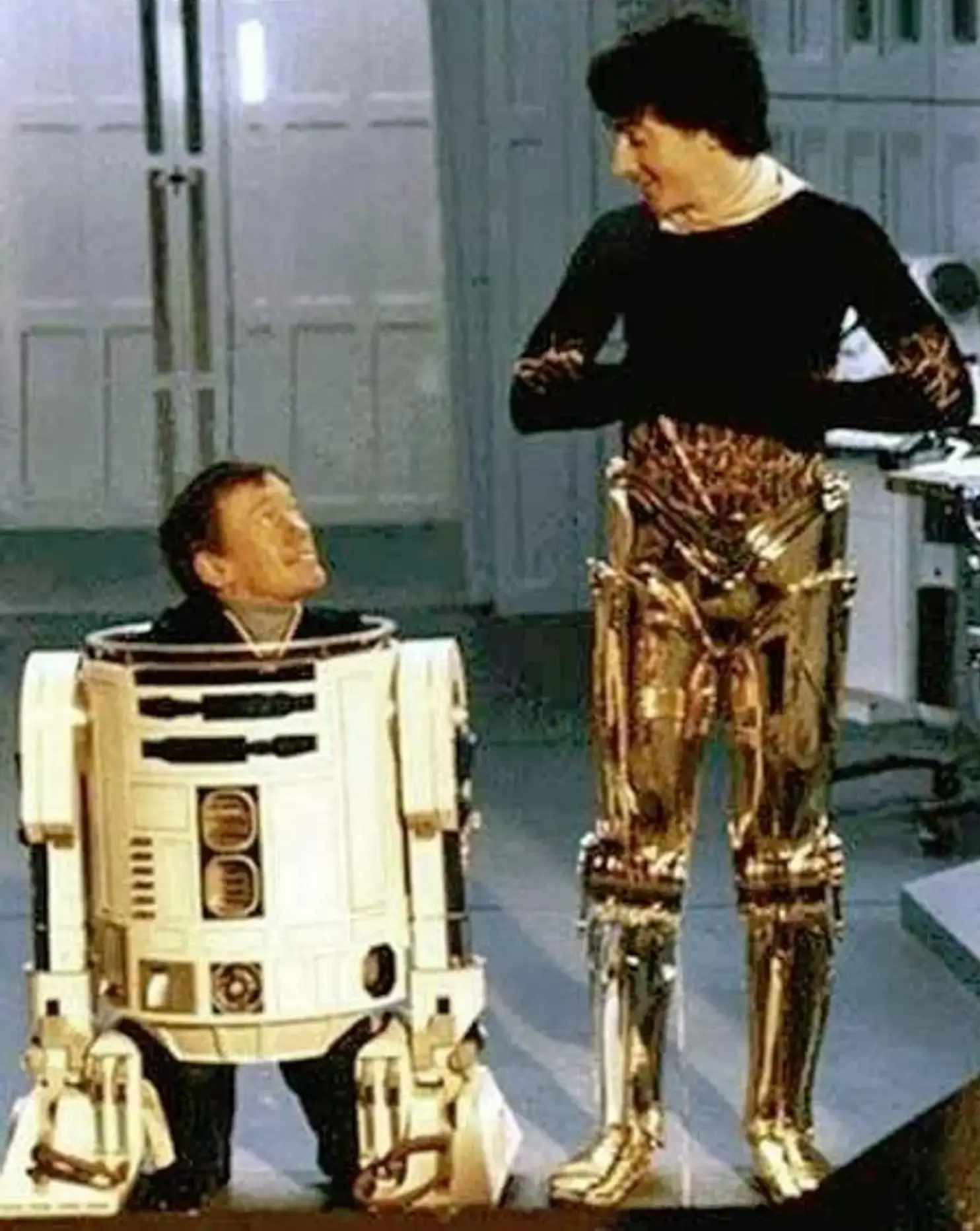 Kenny Baker pokes his head out of the top of his R2-D2 costume, looking up at Anthony Daniels, wearing the legs of this C-3P0 costume.