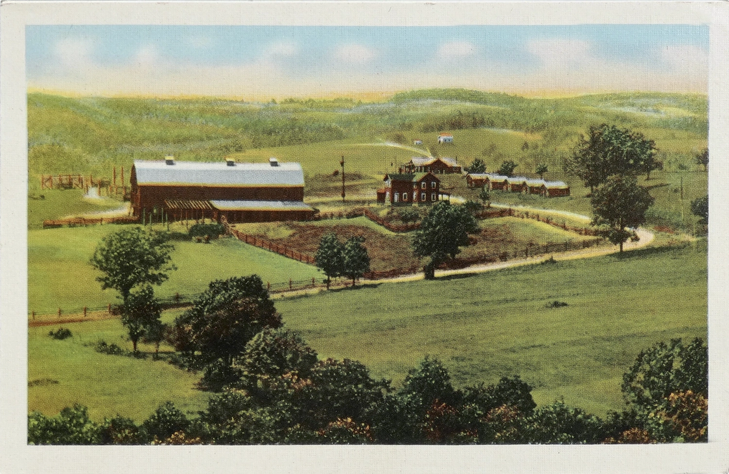 A farm consisting of a large red barn and several farm houses, all surrounded by lush green fields and forest.