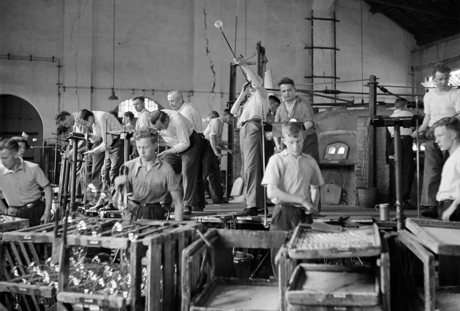 Factory workers blowing glass light bulbs and handling them.